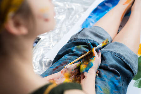 Inspiration and creativity. Cropped shot of female artist taking break, sitting with hands and jeans dirty with colorful paint.の写真素材