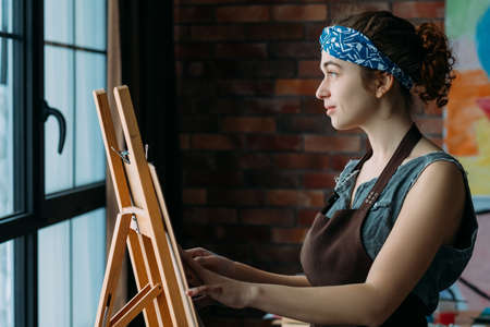 Talent and creativity. Side view of inspired female artist using easel for painting abstract artworks.の写真素材