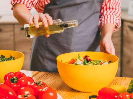 Vegetarian lifestyle. Cropped shot of woman cooking, dressing vegetable salad with organic olive oil.の写真素材