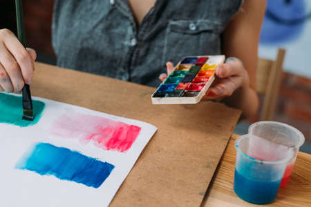Hobby and creativity. Cropped shot of young female artist painting abstract artwork with watercolor.の写真素材