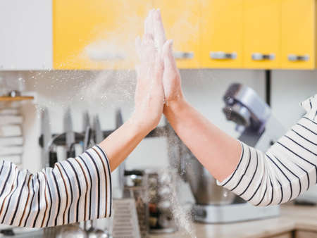 Kitchen team. Assistance and cooperation. Closeup of women hands giving high five, shacking off flour.の写真素材
