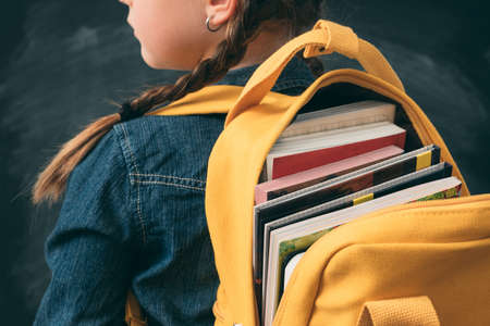 Back to school. Back view of young girl ready to study, with open backpack full with books.の写真素材