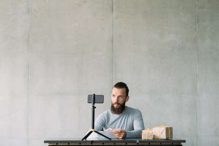 Social media influencer. Hipster guy using smartphone on tripod, reading letters on camera,...