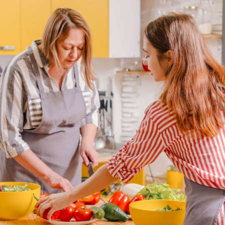 Family cooking hobby. Mother and daughter preparing salad with fresh natural vegetables.