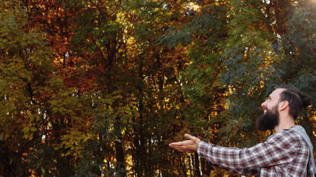 Fall landscape. Side view of happy hipster guy enjoying time in autumn forest. Blur trees and fallen...