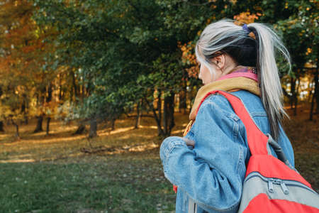 Country tourism. Lady hiking with backpack in autumn nature park. Blur trees and foliage background.の写真素材