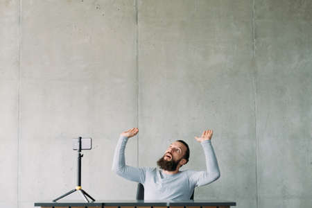 Social pressure. Hipster guy holding hanging over heavy influence load in front of smartphone on tripod. Copy space.の写真素材
