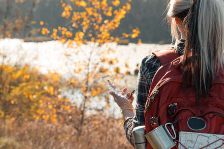 Hiking tourism. Cropped back view of lady using compass to explore country. Swamp and fall landscape background.の写真素材