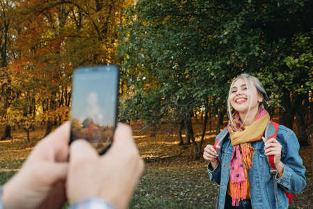 Fall hiking. Man using smartphone camera to take picture of his girlfriend on autumn forest...