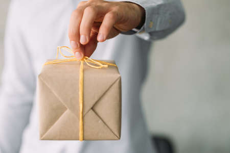 Goods delivery service. Closeup of beige gift box in business man hand. Copy space.の写真素材