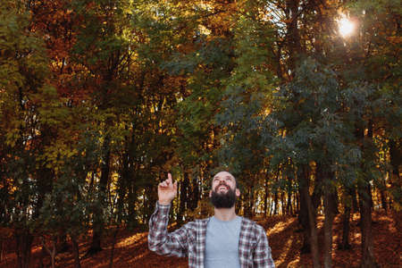 Fall forest. Happy hipster guy pointing finger up in air in nature park. Autumn trees background.の写真素材