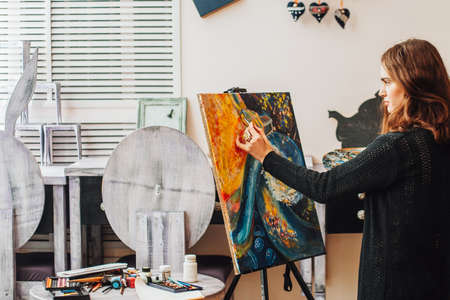 Painting process. Side view of female hipster artist creating colorful abstract painting in studio.の写真素材