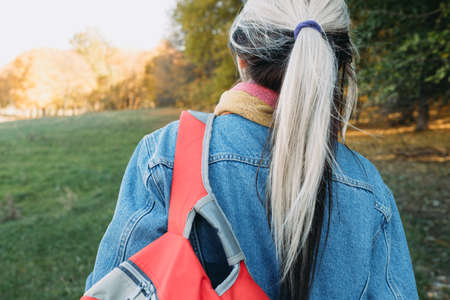 Open air leisure. Back view of lady with backpack in autumn nature park. Blur fall landscape background.の写真素材