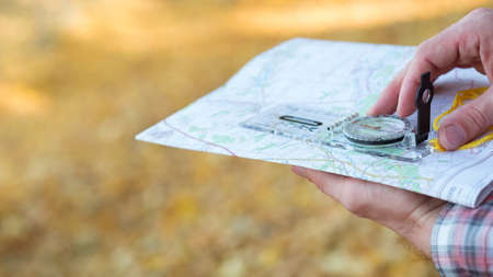 Traveler lifestyle. Closeup of man hands holding compass and map. Blur yellow grass background. Copy space.の写真素材