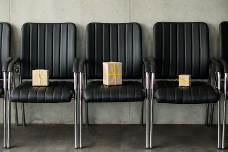 Corporate party celebration. Beige paper gift boxes tied with yellow cord left on office chairs.