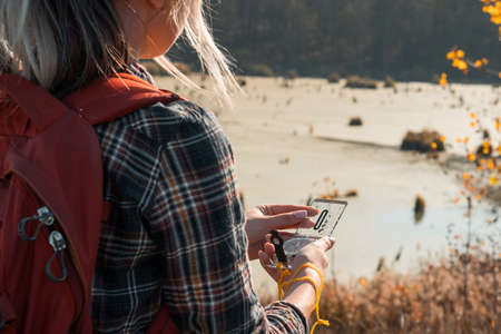 Hiking tourism. Cropped back view of lady using compass to explore country. Swamp and fall landscape...