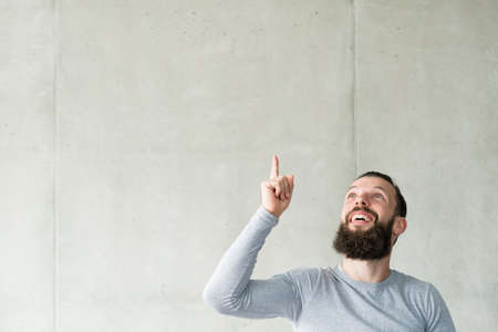 Good news. Important information. Cheerful hipster guy looking up and pointing finger in air. Gray...