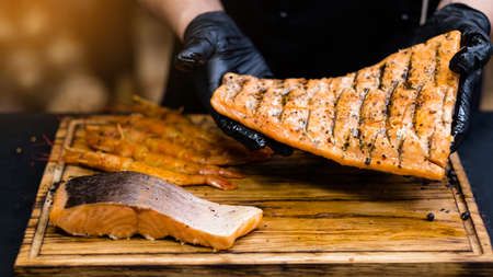 Seafood restaurant. Chef in black cooking gloves holding seasoned smoked salmon tail filletの写真素材