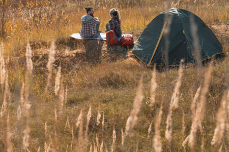 Romantic camping. Back view of couple sitting on ground, talking. Tent, fall nature background.
