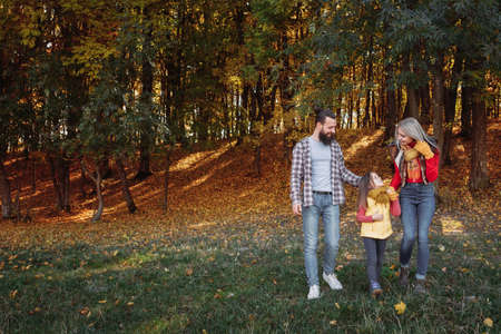 Fall family leisure. Back view of parents walking with daughter in nature park. Trees, faded grass,...