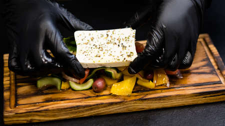 Traditional Greek salad recipe. Chef hands serving feta cheese seasoned with oregano over vegetables on wooden board.の写真素材