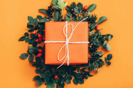 Floral decoration. Handmade gift box with rose hip berries and green leaves on orange background.の写真素材
