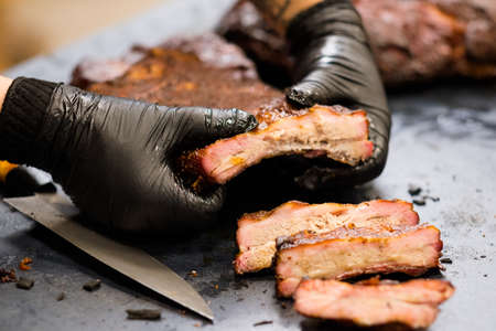 Culinary master class. Chef in black cooking gloves holding smoked pork ribs. Sliced meat and knife on table.の写真素材