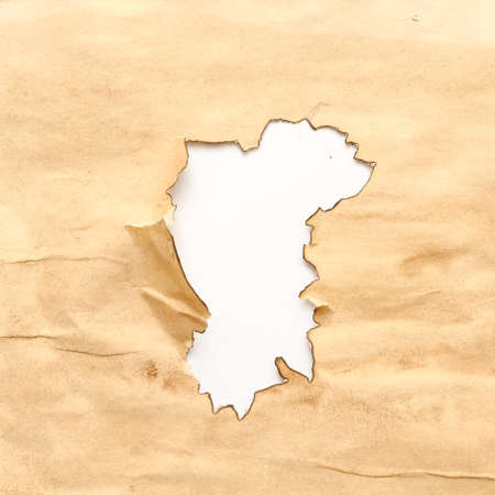 Aged wrinkled beige paper with burnt hole on white background. Grunge abstract design. Copy space.の写真素材