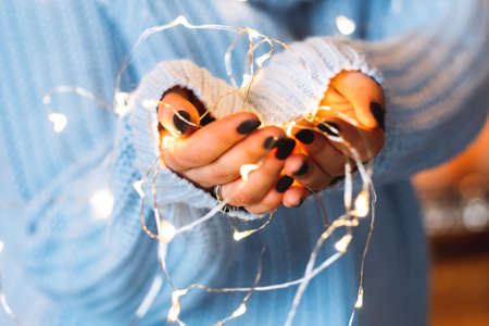 Festive mood. Winter holiday interior decoration. Closeup of white fairy lights in woman hands.