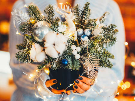 Winter holiday interior decor. Cropped shot of florist holding pot with fir tree twigs and fairy lights.の写真素材