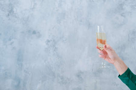 Holiday celebration. Glass of champagne in lady hand over blur textured gray wall background. Copy...