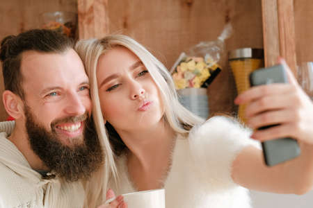 Morning family fun. Closeup portrait of couple drinking coffee in kitchen, using smartphone camera to take selfie.の写真素材