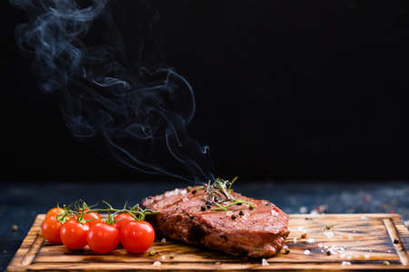 Steakhouse menu. Rib eye steak. Closeup of grilled beef meat with cherry tomatoes and burning rosemary twig. Copy space.の写真素材
