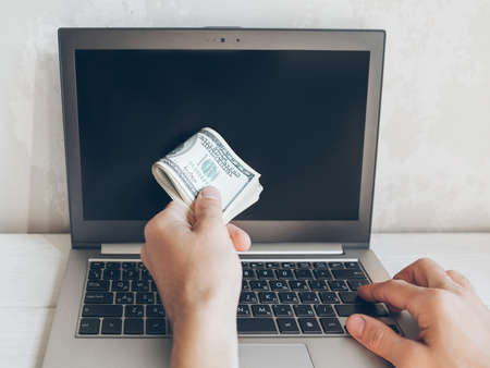 Online banking. Hundred dollar bills, laptop. Male hand with cash money.の写真素材