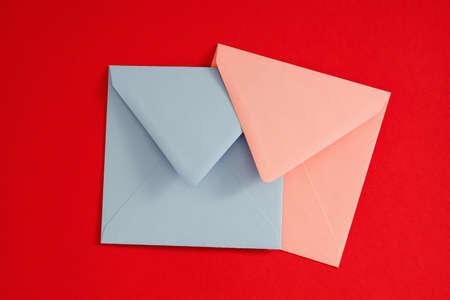 Romantic mail. Flat lay of pale blue and pink blank envelopes on red background. Copy space.の写真素材