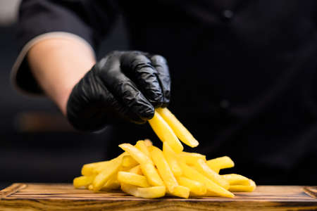 Traditional American fast food restaurant snacks. Cropped shot of chef in cooking gloves serving french fries on wooden board.の写真素材