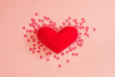 Romantic greeting card. Flat lay of red handmade felt heart on pastel pink background. Copy space.