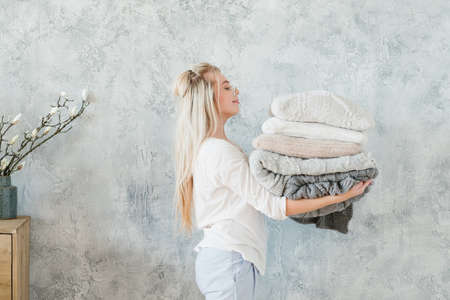 Cozy winter bedding. Happy housewife with warm knitted blanket and pillow stack.