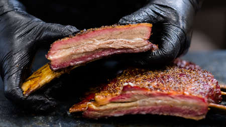 Culinary master class. Closeup of chef hands in black cooking gloves holding smoked beef ribs.の写真素材