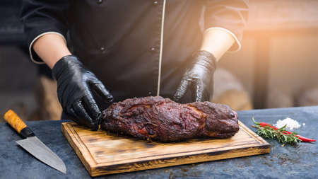 Grill restaurant kitchen. Closeup of chef hands in black cooking gloves serving smoked pork neck.の写真素材