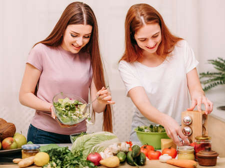 Family unity. Cooking leisure. Two sisters making salad with organic food ingredients in kitchen.の写真素材
