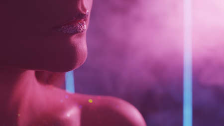 Color smoke face. Night glam. Woman with glitter lips bare shoulder in purple neon light.の写真素材