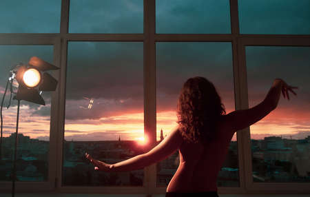 Sensual sunset. Spiritual tranquility. Nude woman silhouette dancing in spotlight over teal red sky in studio window.の写真素材