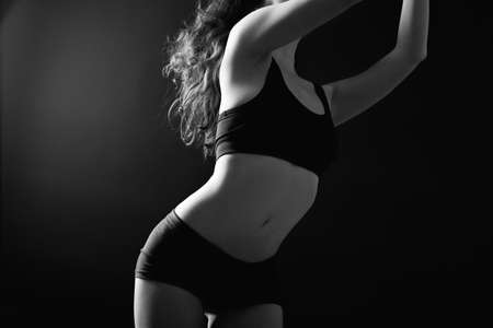 Female perfection. Body care. Flexible woman torso silhouette in black athletic underwear isolated on dark.の写真素材