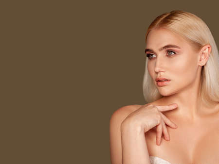 Pretty woman portrait. Laser therapy. Blonde lady with perfect skin holding orchid flower isolated on brown.の写真素材