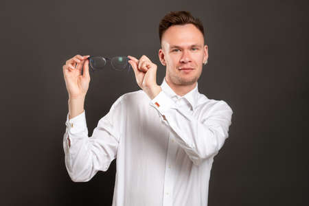 Vision correction. Laser eye surgery. Confident hipster guy happy to take off eyeglasses isolated on dark. Satisfied man enjoying perfect eyesight. New perspective view.の写真素材