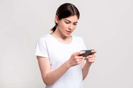 Mobile game. Online entertainment. Enthusiastic woman enjoying playing on smartphone isolated on...