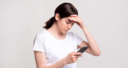 Social media anxiety. Internet stress. Troubled woman reading disturbing news on smartphone isolated on neutral copy space. Online conflict. Negative chat.の写真素材
