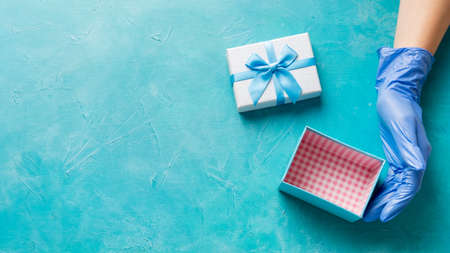 Gift delivery. Holiday surprise. Empty present box hand in medicine gloves on textured blue copy...