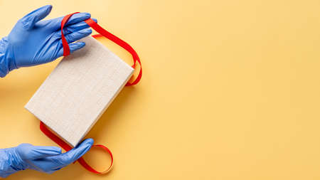 Disease protection. Gift delivery. Hands in medicine gloves opening present box. Isolated on beige...